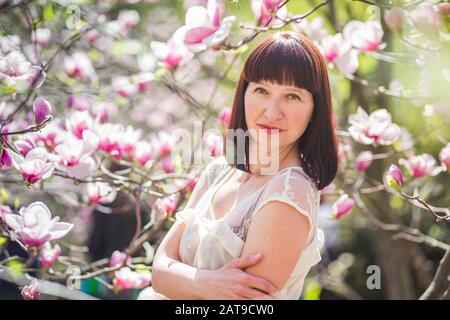 beautiful dark-haired woman among branches of magnolia. first flowers in trees in spring. Stock Photo