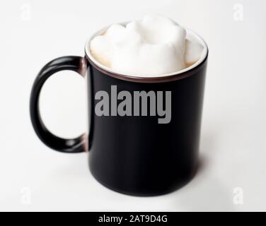 Black coffee mug with frothed milk mockup with room for text or art isolated on a light background.  This beverage is a latte cup of coffee in a black Stock Photo