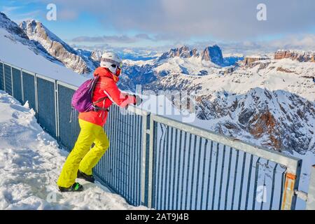 Woman skier taking a break and enjoying the mountain views towards Sassolungo and Sella group in Dolomites, Italy, from a viewpoint at Serauta cable c Stock Photo