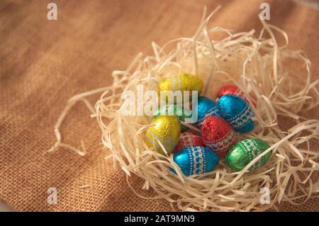 Close-up of some Easter eggs of different colors in a nest of natural straw on an also natural jute surface. In the image there is space for texts or Stock Photo