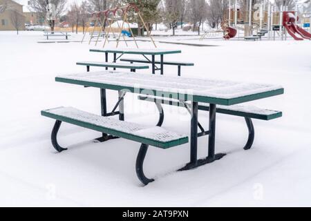 Snowy picnic tables and benches at a park blanketed with snow in winter Stock Photo