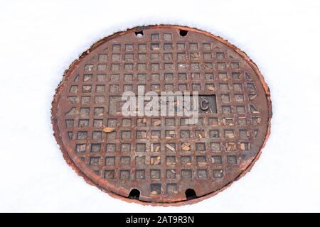 Rusty circular utility electric manhole cover amid fresh white snow in winter Stock Photo