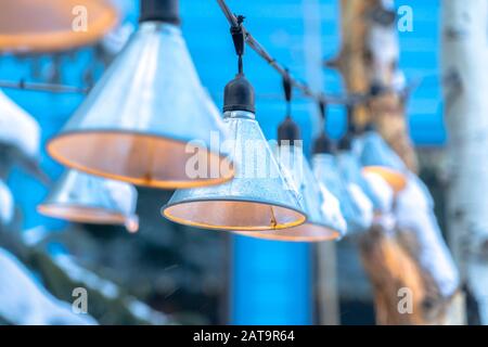 Cone shaped lamps hanging on black electric string wires against blurry sky Stock Photo