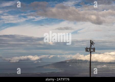 Kahului, Maui,, Hawaii, USA. - January 13, 2020: Different layers of clouds in blue sky over land and ocean with mountains on horizon. Electrical pole Stock Photo