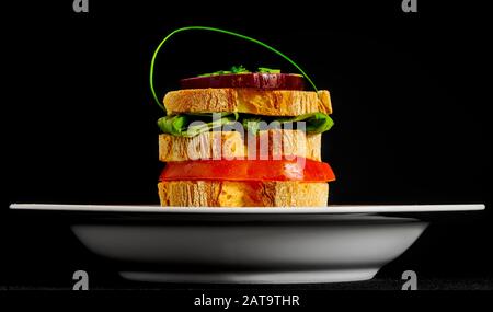 Rustic sandwich on a white ceramic plate: sliced bread, tomato, lettuce salad, red Tropea onion, chives, mayonnaise. Stock Photo