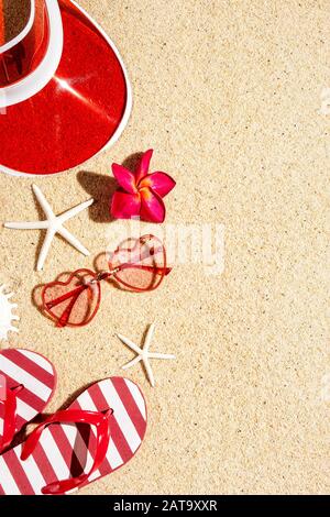 Sunglasses, flip flops, plastic cap in red color on sand, top view with copy space, summer holiday concept, vertical composition Stock Photo