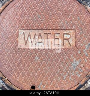 Square frame Removable circular water supply manhole cover against road and rocky ground Stock Photo