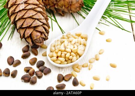 Peeled kernels of cedar nuts in a spoon, two pinecones and nuts in the shell against a light wooden board Stock Photo