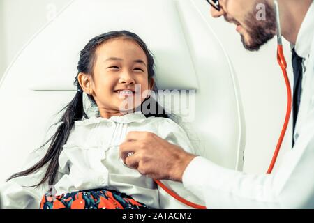 Young male doctor examining little kid in hospital office. The kid is happy and not afraid of the doctor. Medical children healthcare concept. Stock Photo
