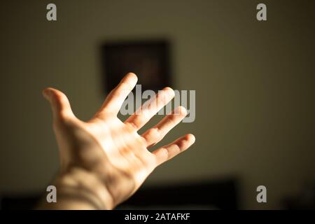 man extended his hand and holds the palm of his hand wide open as the sun shines on it through window blinds on a sunny day. Stock Photo