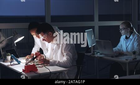 Multiracial man and woman checking motherboard with multimeter tester in electronics laboratory. They discussing and explaining different things Stock Photo