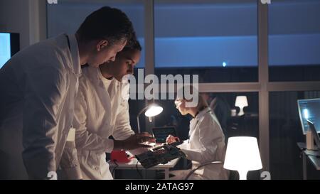 Side view of two Electronics Development Engineers talking about motherboard and explaining details of their project in electronics lab. Multiracial team work Stock Photo