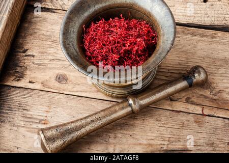 Raw organic red saffron spice on wooden background.Vintage metal mortar with pestle Stock Photo