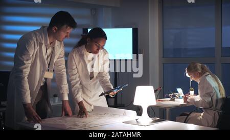 Man and woman in lab coats working in electronics lab with motherboard and control electronics scheme discussing the way of their improvement Stock Photo