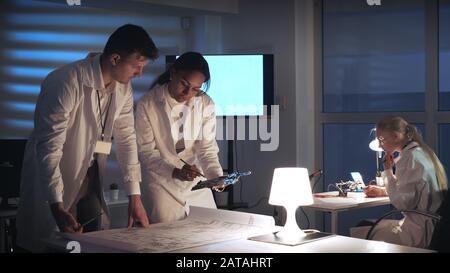 Man and woman in lab coats working in electronics lab with motherboard and control electronics scheme discussing the way of their improvement Stock Photo