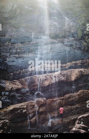Local man standing in front of a beautiful waterfall in Knuckles range, Sri Lanka Stock Photo