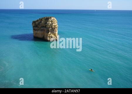 Elevated view of a young man on a paddleboard near a majestic sea stack. Praia do Barranquinho, Lagoa, Algarve, Portugal. Stock Photo