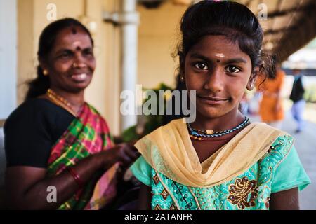 A young girl in traditional dress from Sri lanka poses at the train station while her mother smiles behind her. Stock Photo