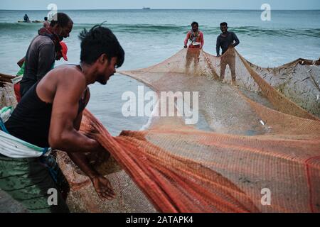 Fishermen pulling the nets out of the ocean on the beach in Sri Lanka. Town of Trincomalee has big and long beach where locals pull nets and fish. Stock Photo