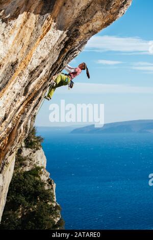 Young female climber climbing a clif above the Adriatic sea in Croatia. Stock Photo