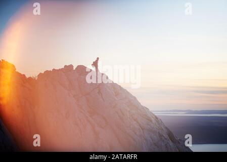 A hiker standing on a ridge of a mountain and looking at the sunset over the Adriatic sea. Paklenica National Park, Croatia. Stock Photo