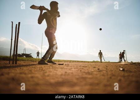 Boys playing cricket on the field in Sri Lanka with sunset behind them. Stock Photo