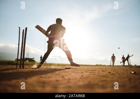 Boys playing cricket on the field in Sri Lanka with sunset behind them. Stock Photo