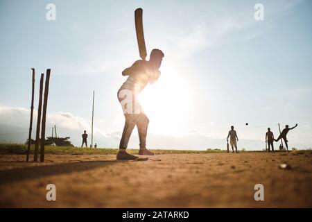 Boys playing cricket on the field in Sri Lanka with sunset behind them. Stock Photo