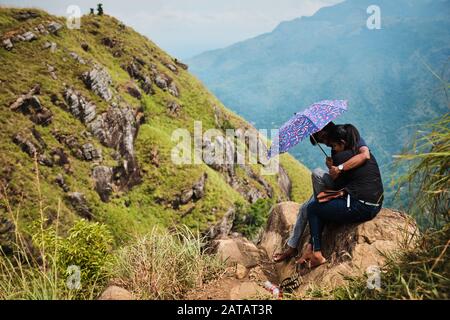 Sri Lankan man and woman hugging under the umbrella on Little Adams peak near Ella, Sri Lanka Stock Photo