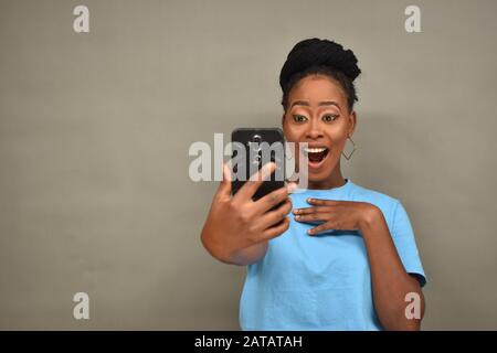 pretty african woman viewing content on her mobile phone feeling happy and excited, looking surprised Stock Photo
