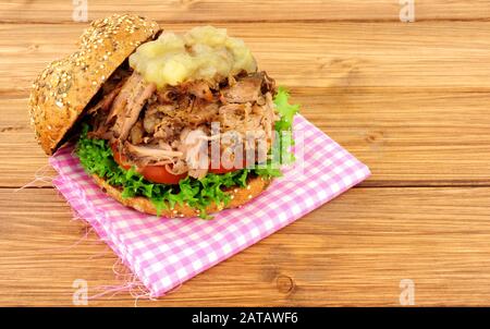 Hog roast meat sandwich with apple sauce and salad in a seed covered bread roll on a wooden background Stock Photo