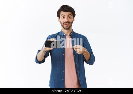 Technology, advertisement and people concept. Attractive surprised excited man with beard, telling about interesting app or news heart online, pointin Stock Photo