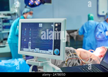 Electrocardiogram in hospital surgery operating emergency room showing patient heart rate with blur team of surgeons background. Stock Photo