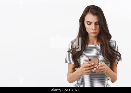 Serious-looking, concerned young woman receive disturbing message, reading text with focused, determined and troubled expression, watching video Stock Photo
