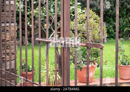Metal gate with doors that have an iron lock with sliding and locking bar and vertical bars oxidized by the passage of time. Stock Photo