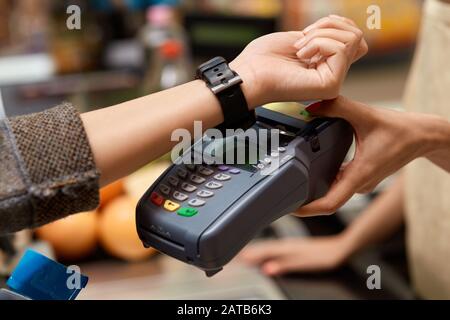 Daily Shopping. Woman standing at the supermarket cashier counter paying for purchases contactless with smartwatch close-up Stock Photo