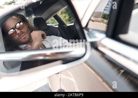 Young adult man sitting in car, looking in mirror Stock Photo