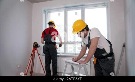Apartment repair in the room - two men workers measuring the window and writing notes about it Stock Photo