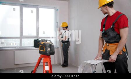 Two men workers measuring the distance from the windowsill to the ceiling and another writing notes about it Stock Photo