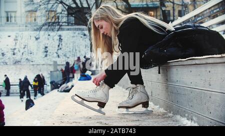 A young woman with blond hair tie up her figure skates before walking out on the rink Stock Photo