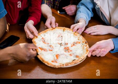 Hands of diverse people taking pizza slices from wooden board dining together, multiracial friends or colleagues sharing meal having lunch in cafe res Stock Photo