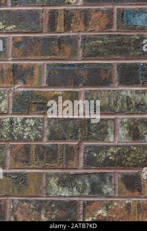 A vertical close-up section of weathered, multi-colored brick wall; background. Stock Photo