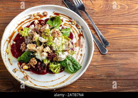 Beetroot carpaccio with walnuts, goat cheese, lettuce and spinach. Dressed with sauce. In a deep plate, on a dark background. Copy space Stock Photo