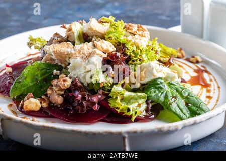 Beetroot carpaccio with walnuts, goat cheese, lettuce and spinach. Dressed with sauce. On a dark background. Copy space Stock Photo