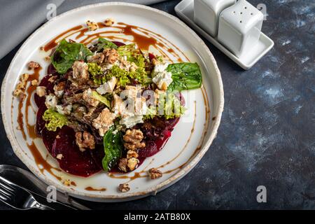 Beetroot carpaccio with walnuts, goat cheese, lettuce and spinach. Dressed with sauce. On a dark background. Copy space Stock Photo