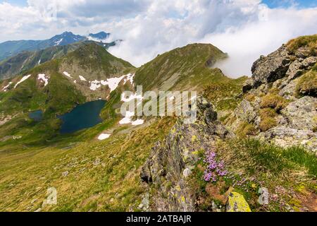 great summer scenery of high mountain range with alpine lake. steep slopes with rocks, grass and spots of snow. clouds on the blue sky. explore fagara Stock Photo