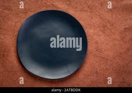 black ceramic plate with an irregular edge on a brown, textured, handmade paper  with a copy space Stock Photo