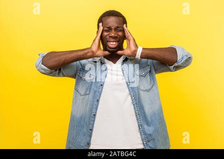 Intense headache. Portrait of unhealthy sick man in denim casual shirt clutching his head, grimacing from unbearable head pain, suffering migraine. in Stock Photo