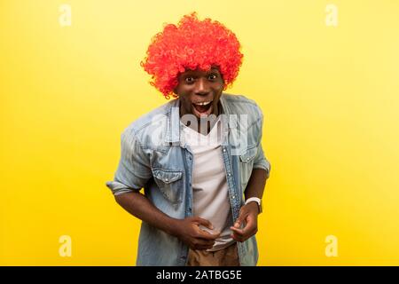 Portrait of enthusiastic funny crazy carefree man wearing red curly wig and denim casual shirt laughing loud at camera, easy optimistic lifestyle. ind Stock Photo