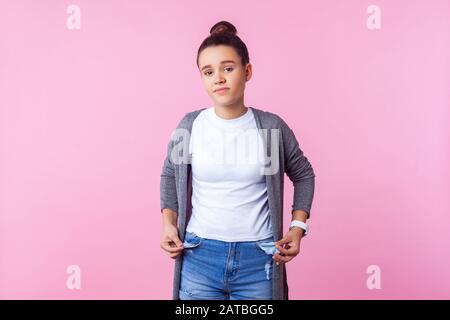 Portrait of frustrated brunette teenage girl with bun hairstyle in casual clothes showing empty pockets inside out, poor has no money, allowance. indo Stock Photo